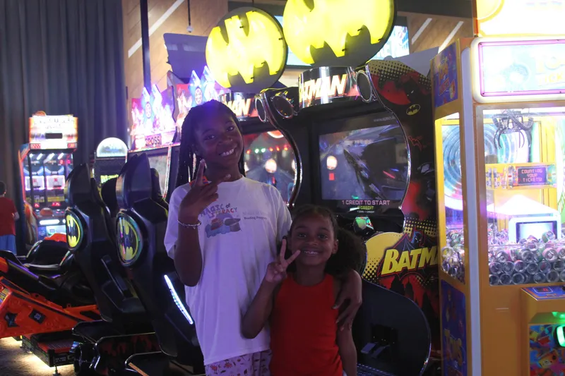 Two young readers posing together in front of a Batman arcade game