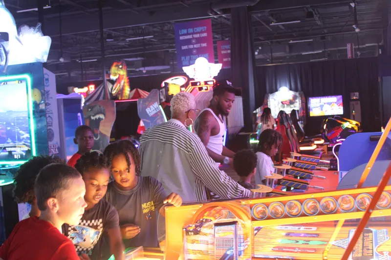 Kids gathered around an arcade game with adults looking on
